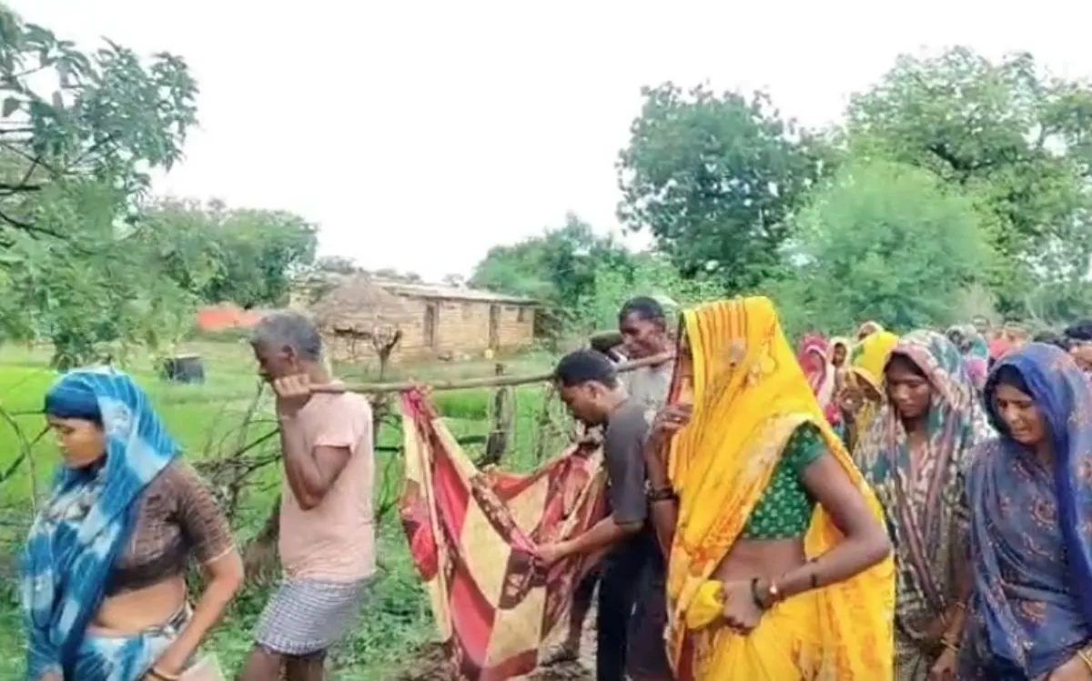 कीचड़ भरे रास्ते से बीमार बच्चे को कपड़े की पालकी में ले जाते ग्रामीण
